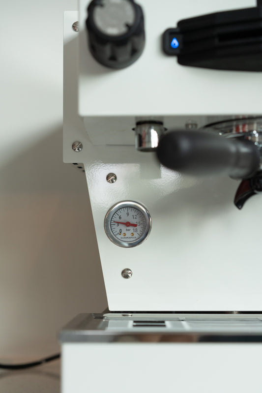 Close up van een La Marzocco espresso machine in het wit. manometer in beeld.